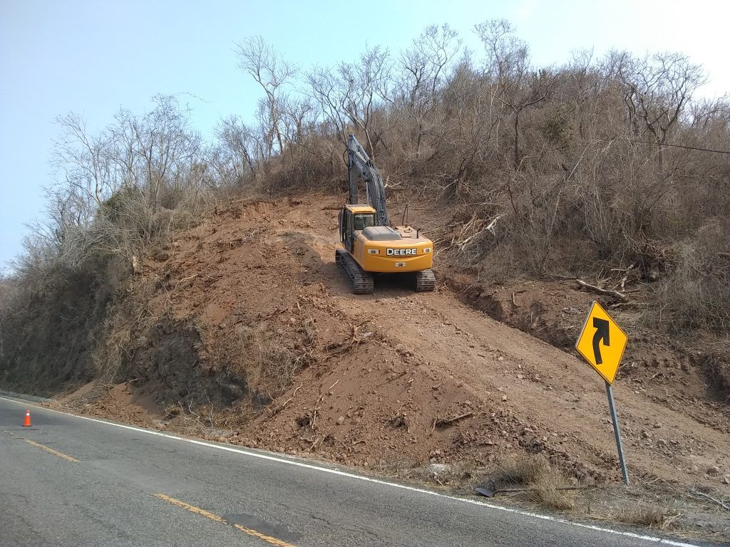 Excavadora trabajando sobre el talud junto al carril de circulación.