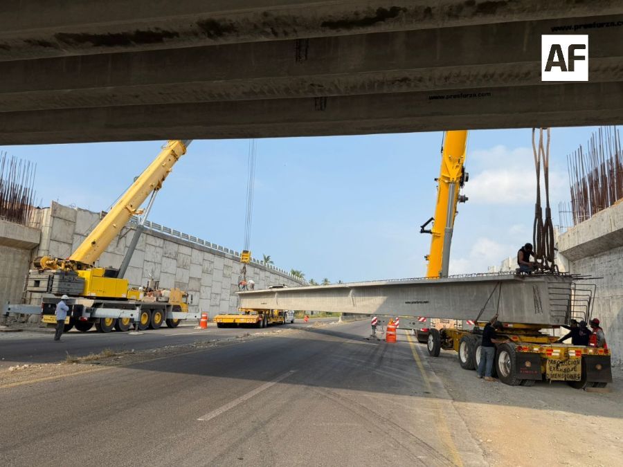 Grúas levantan una trabe de concreto junto a un puente de la autopista Colima–Manzanillo.