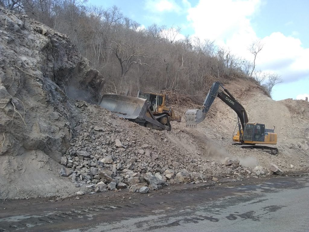 Dos excavadoras trabajan en el corte de un talud junto a la carretera.