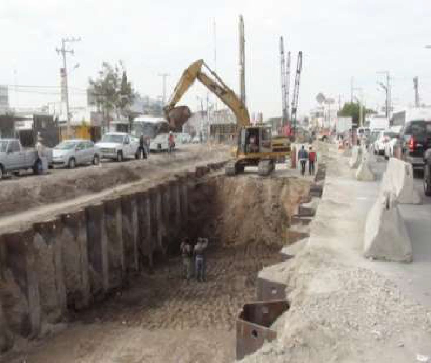 Zanja con entibado y excavadora en el camellón de una avenida.