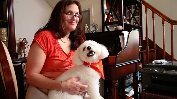 Maria, who lives with MS, sitting at her home desk with a small dog in her lap.