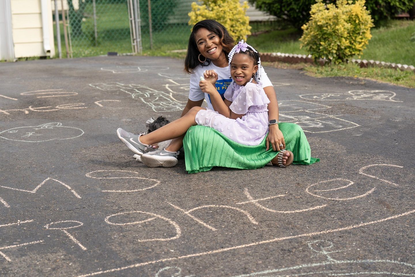 Kresence, a woman who lives with MS, poses with her daughter in her driveway, which is covered with chalk drawings, including the words "MS Fighter."