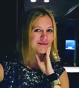 A blonde woman smiles as she holds her chin