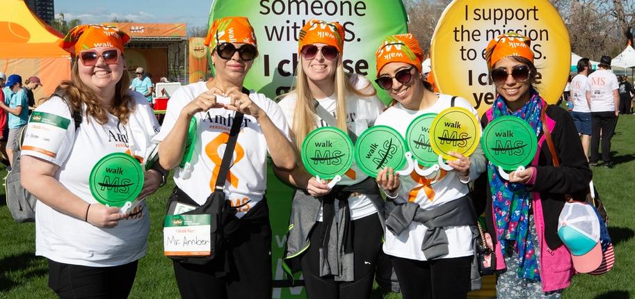 Five women stand side by side posing for a photo while holding green and yellow Walk MS signs.