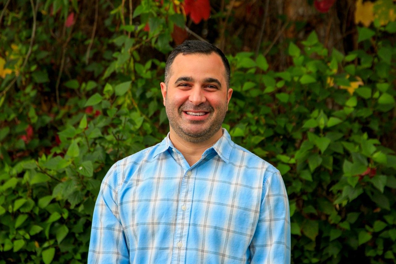 A man stands in front of a hedge.