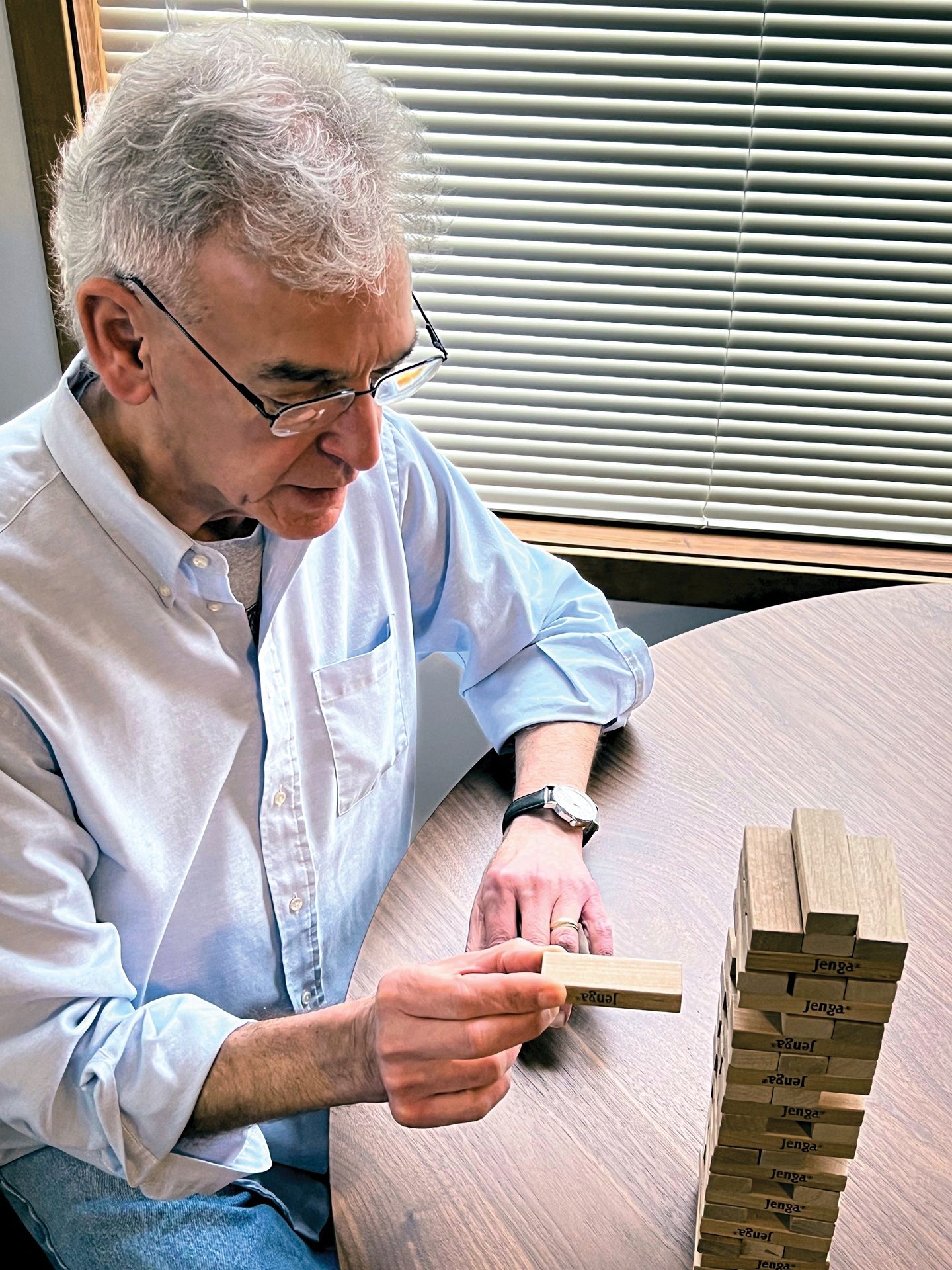 An elderly man engaged in play, arranging colorful wooden blocks on a table with focus.