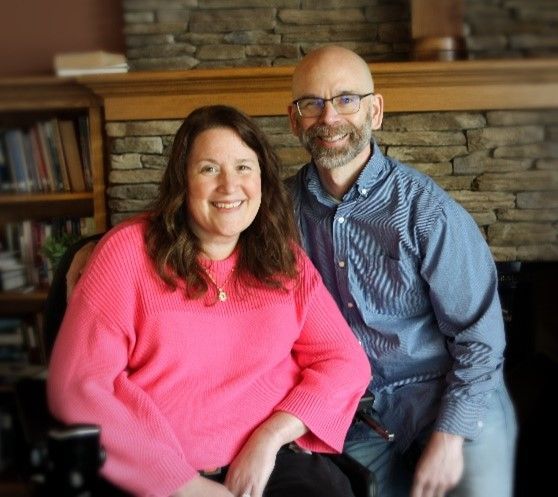 A couple poses in front of a stone fireplace in their living room.
