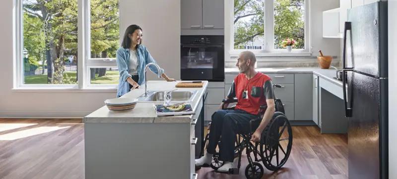 A woman and a man in a wheelchair in a kitchen at Harmon Apartments