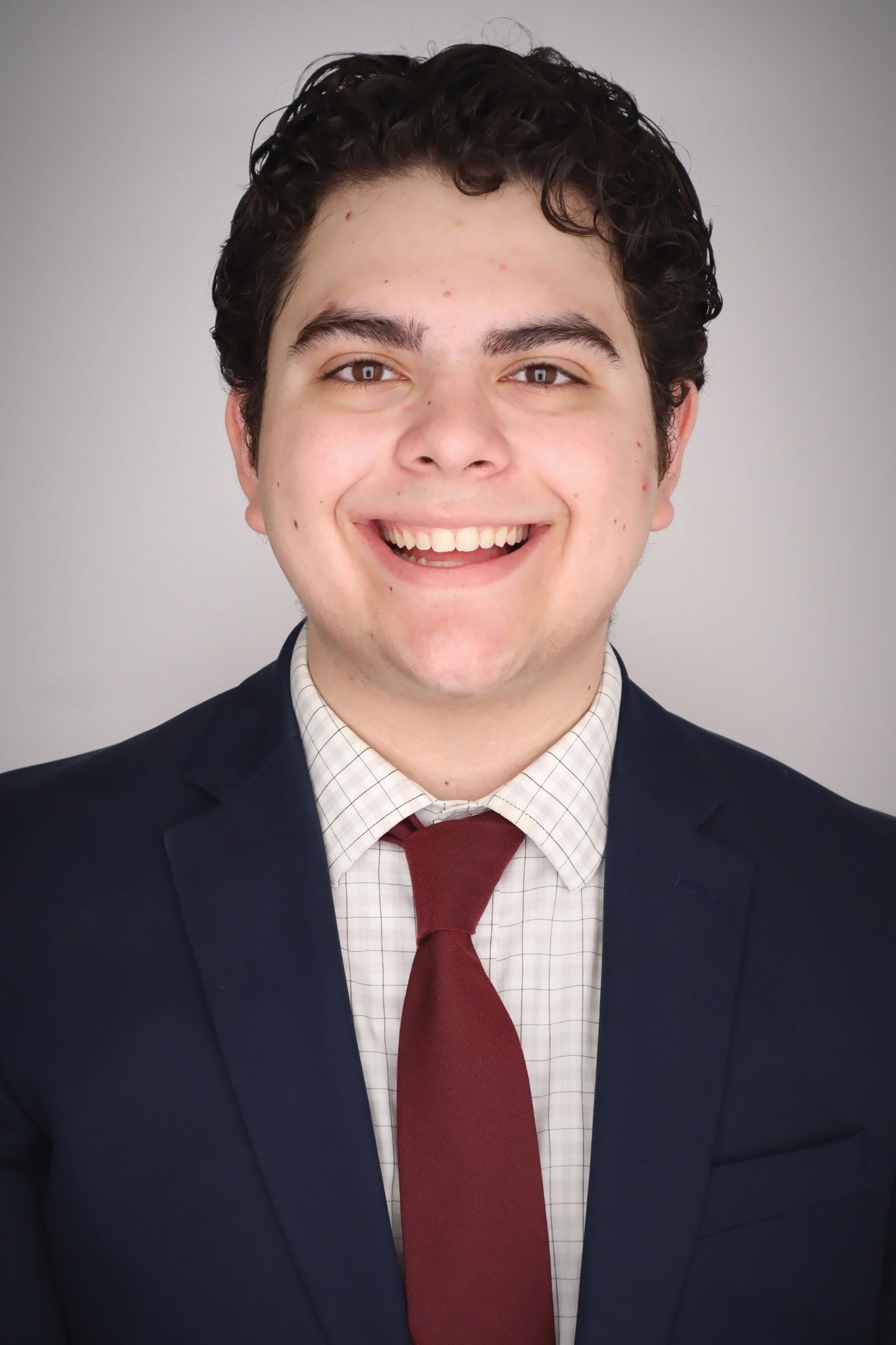 A young man wearing a suit and tie, smiling warmly at the viewer.