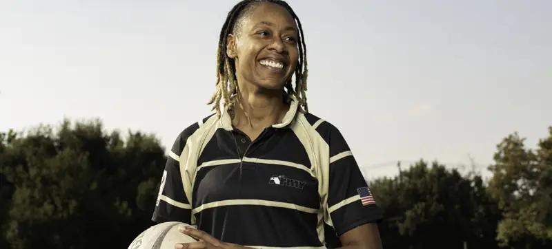 Tra wearing a black and gold polo shirt with trees in the back ground