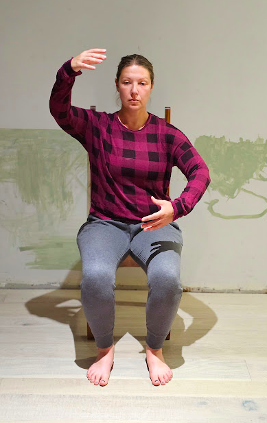 A woman completes a ballet pose while seated in a chair.