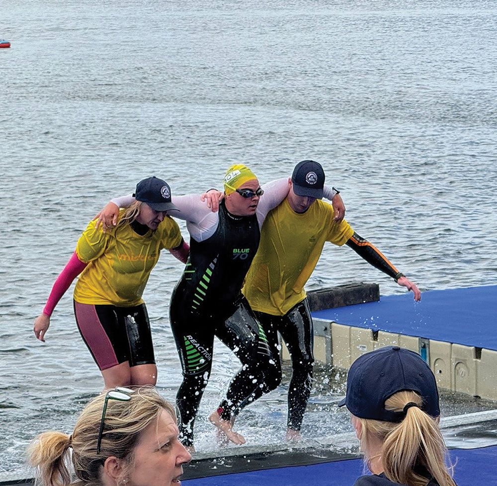 Two people support Rachel Watts as she exits the water.