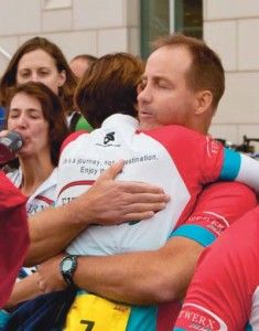 A man and a woman in cycling jerseys hug while standing next to others.