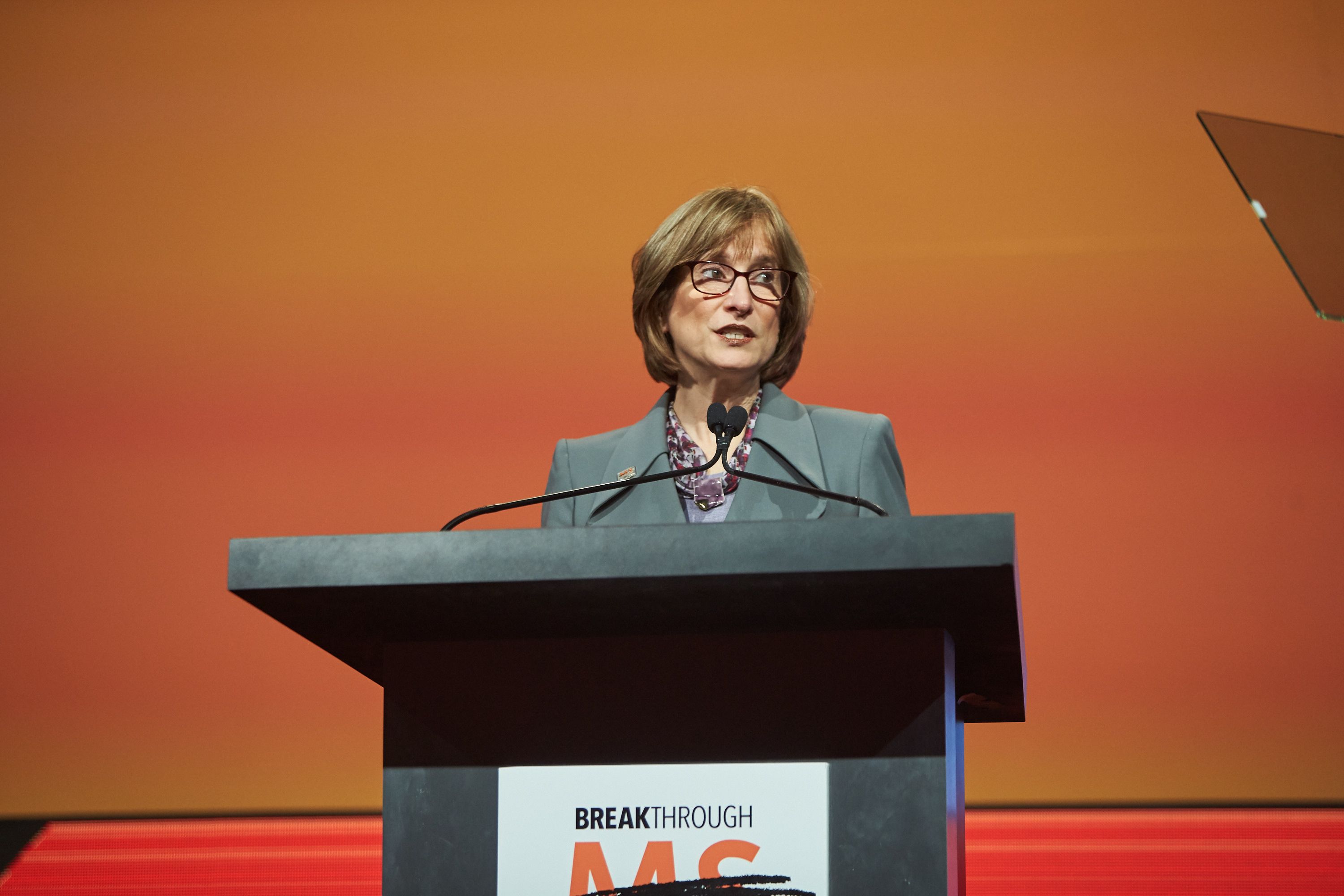 Cyndi Zagieboylo speaks at a podium. A sign in front reads Breakthrough MS