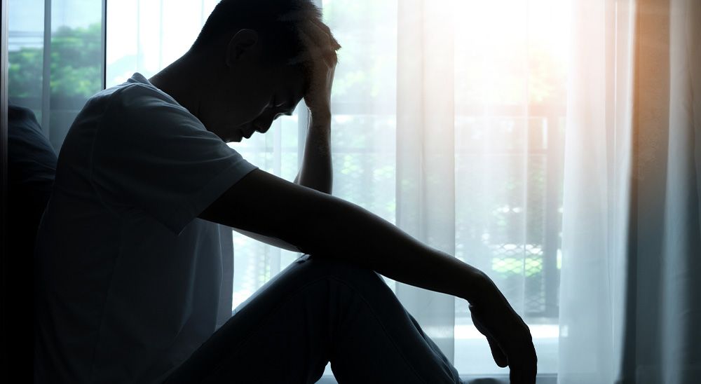 A man sits by the window with his head down.