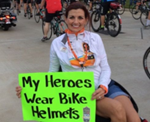 Lisa Sailor holds a sign saying, “My heroes wear bike helmets,” at a Bike MS event.
