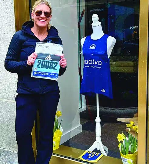 Wendy Haase holds her marathon number next to a window display featuring a Saatva-branded tank top