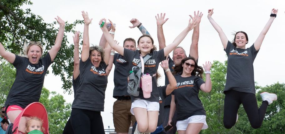 A group of people in black “Keep S’Myelin” t-shirts jump into the air.
