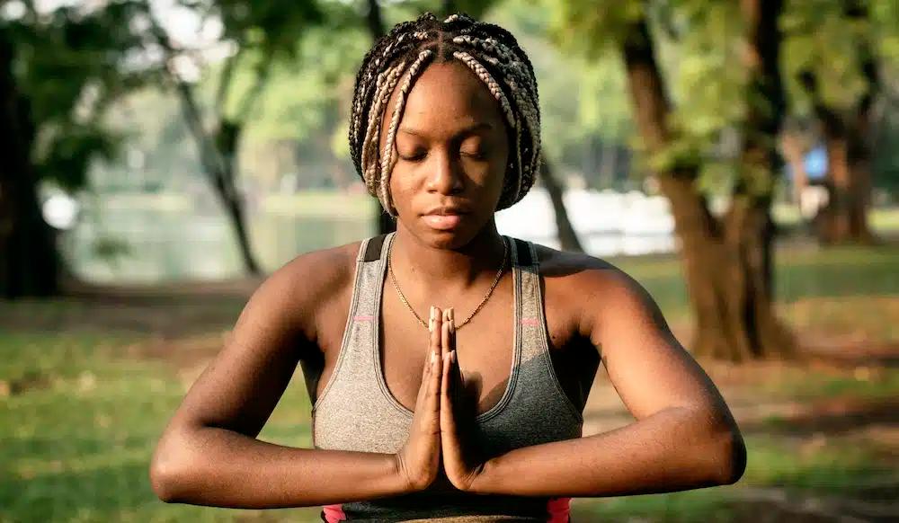A young, Black woman sits in a yoga pose with her eyes closed.