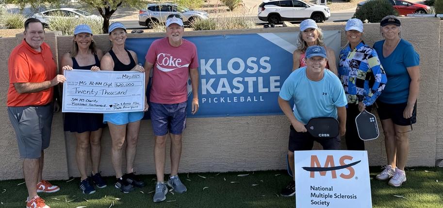 A group of eight people stands in front of a sign reading "Kloss Kastle Pickleball," two women holding a check for $20,000.