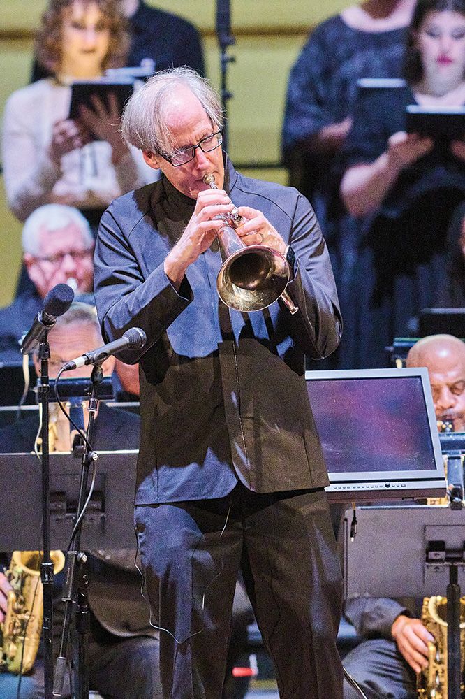 Jeff Beal plays a trumpet at the front of an orchestra.