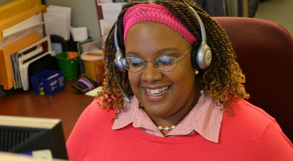 A woman sitting at a computer speaks into a headset.