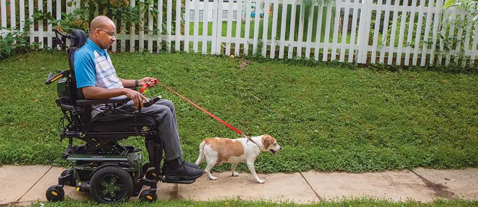 A black man in motorized wheelchair walking a small brown and white dog
