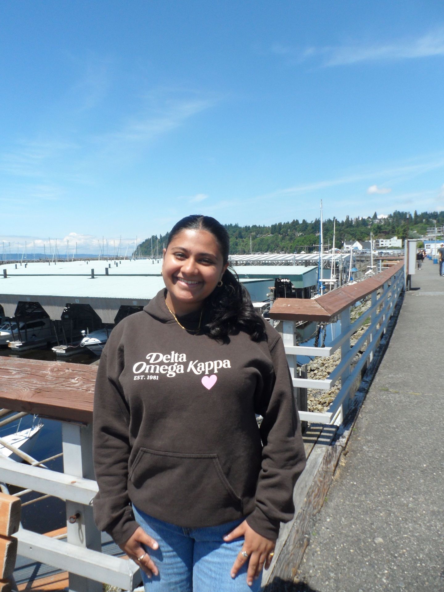A young woman poses on a pier with boats.