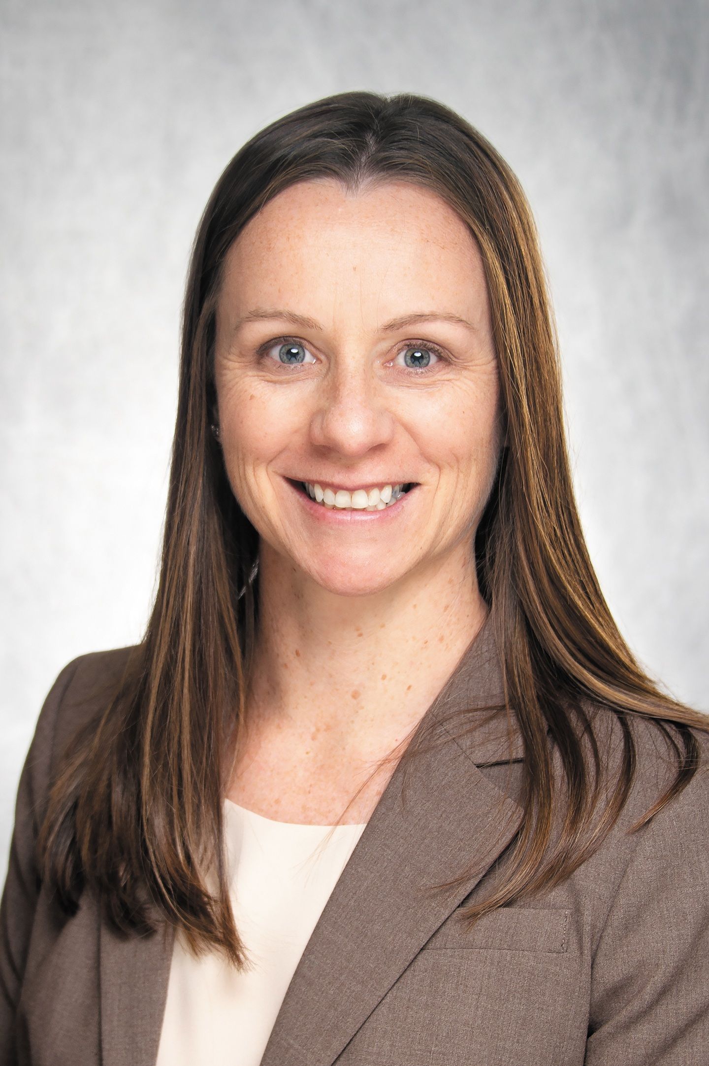 Headshot of a white woman with long, brown hair in a brown jacket and beige shirt.
