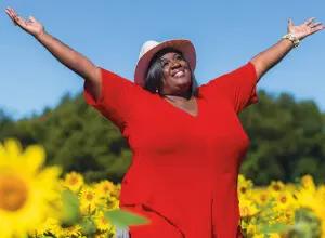 Nicole White with arms raised in a field of sunflowers