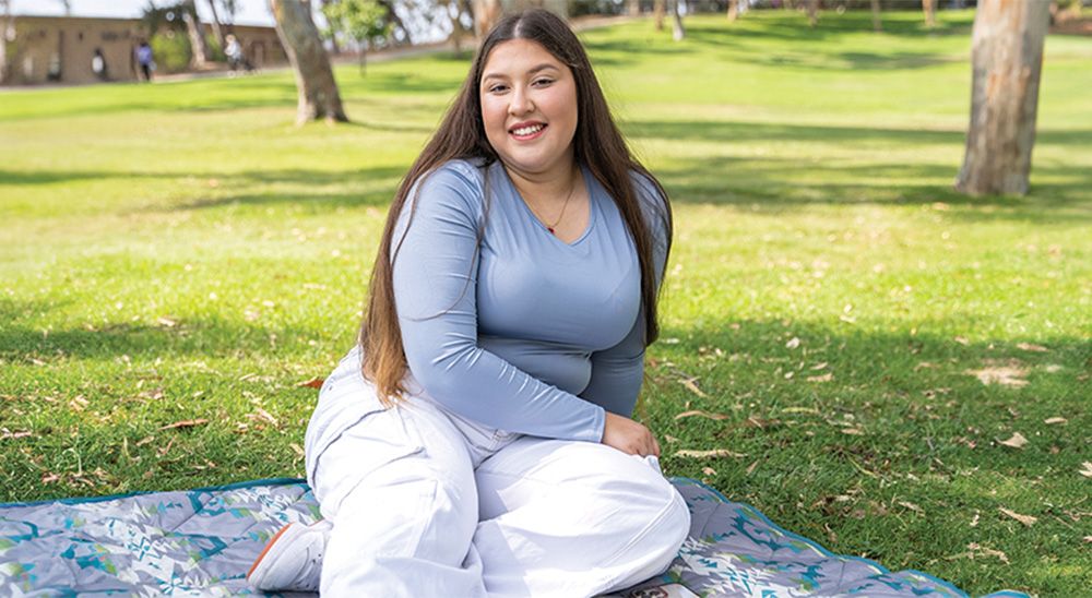 A young woman sits outside on a picnic blanket.