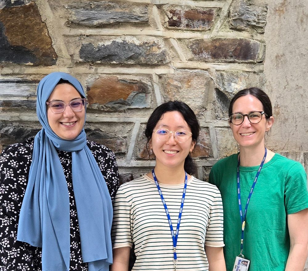 Three women pose in front of a brick wall.