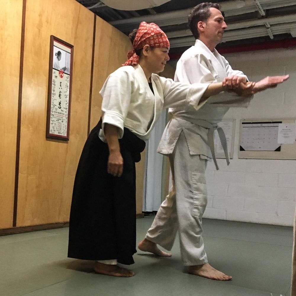 Two individuals perform martial arts while wearing white apparel.
