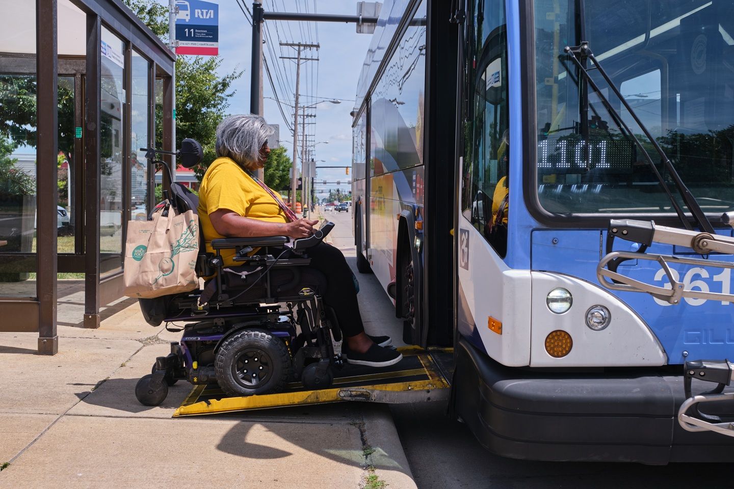 A woman who lives with MS rides her electric wheelchair to the lift on a public bus.