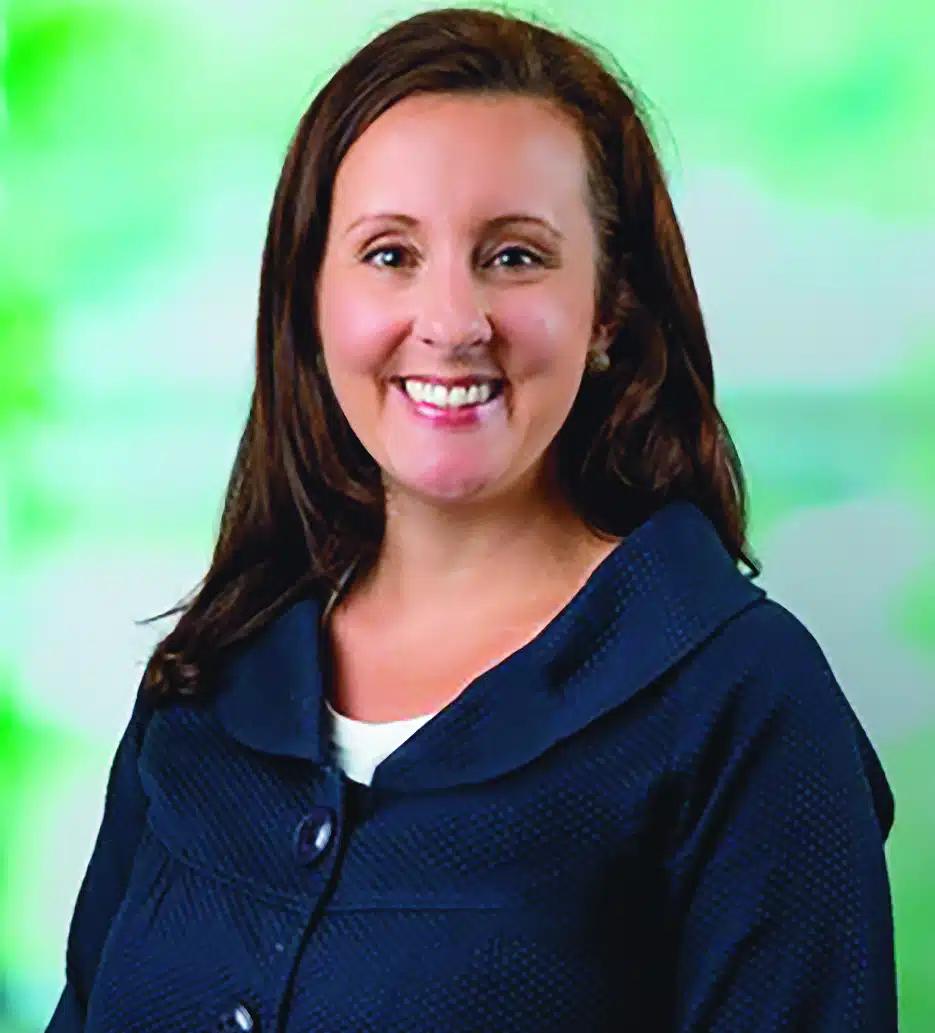 A brunette, Caucasian women smiles at the camera. She is posed in front of a green background.