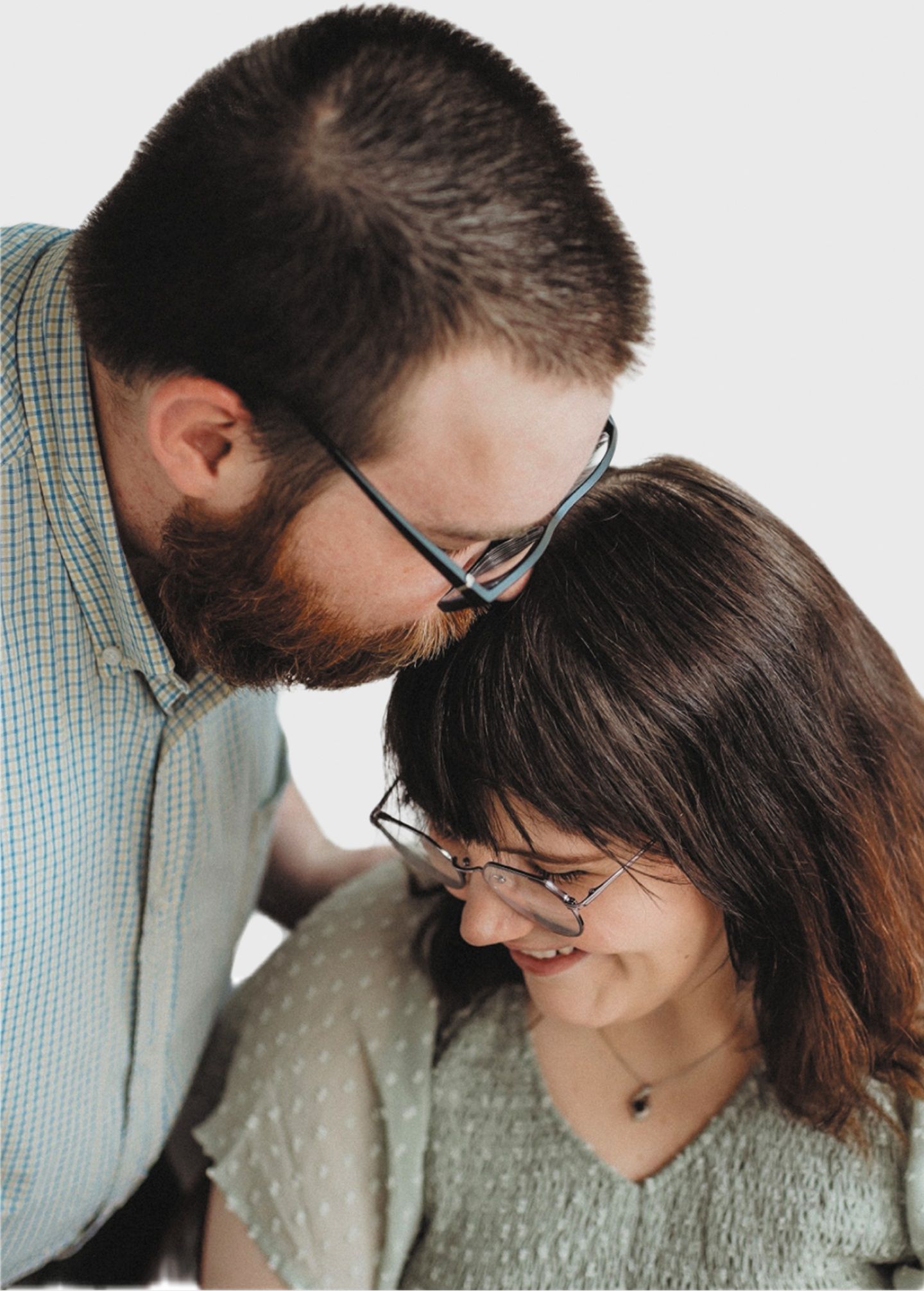 A man leans down to kiss a woman's head, both smiling at each other affectionately.