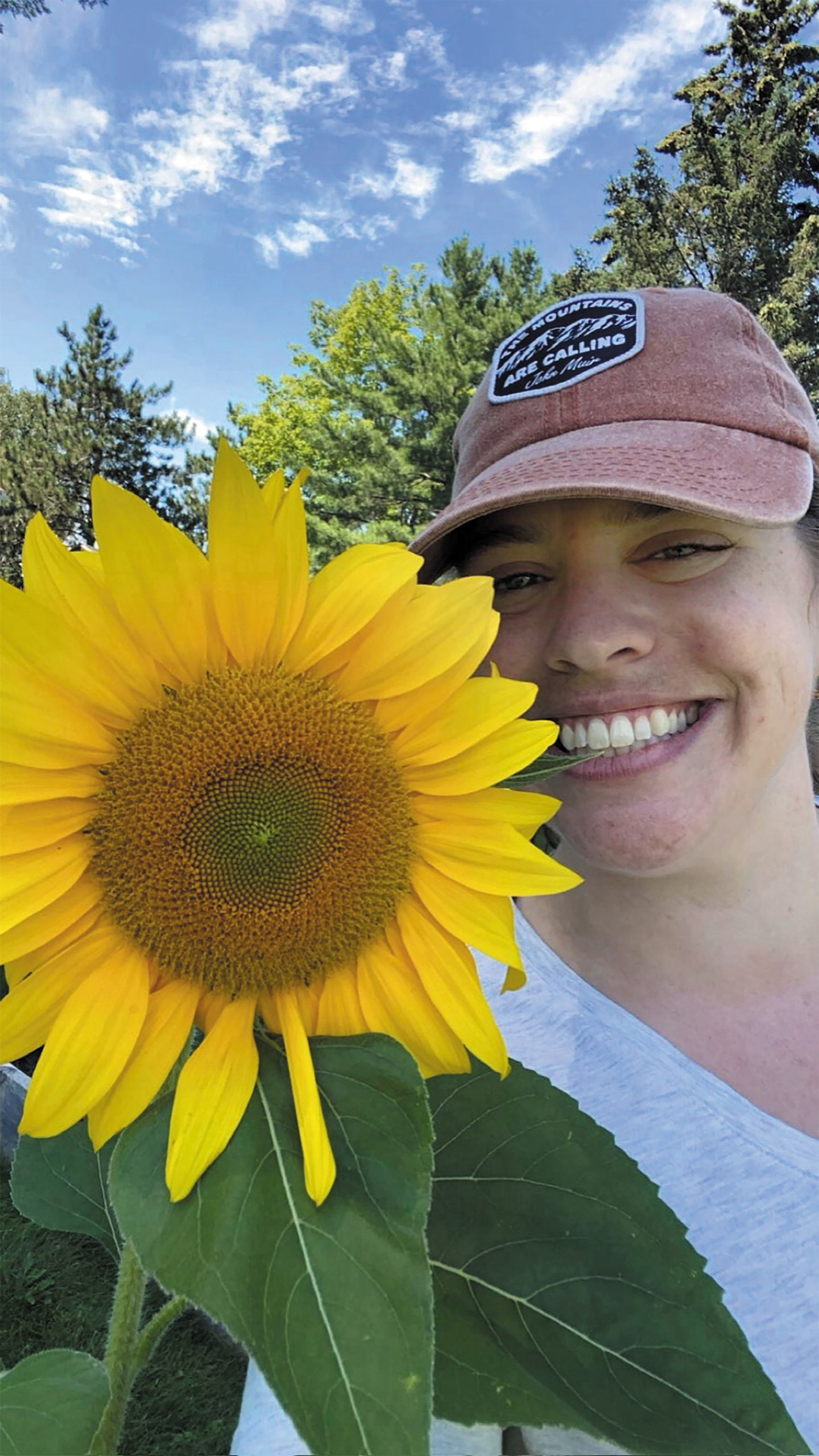 A woman in a hat holds a vibrant sunflower, smiling as she enjoys a sunny day outdoors.