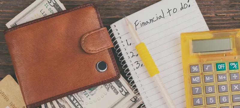 A wallet with $5 bills visible, a financial notepad and pen, and a calculator