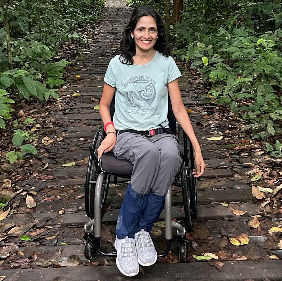 A woman using a wheelchair poses on an outdoor path.