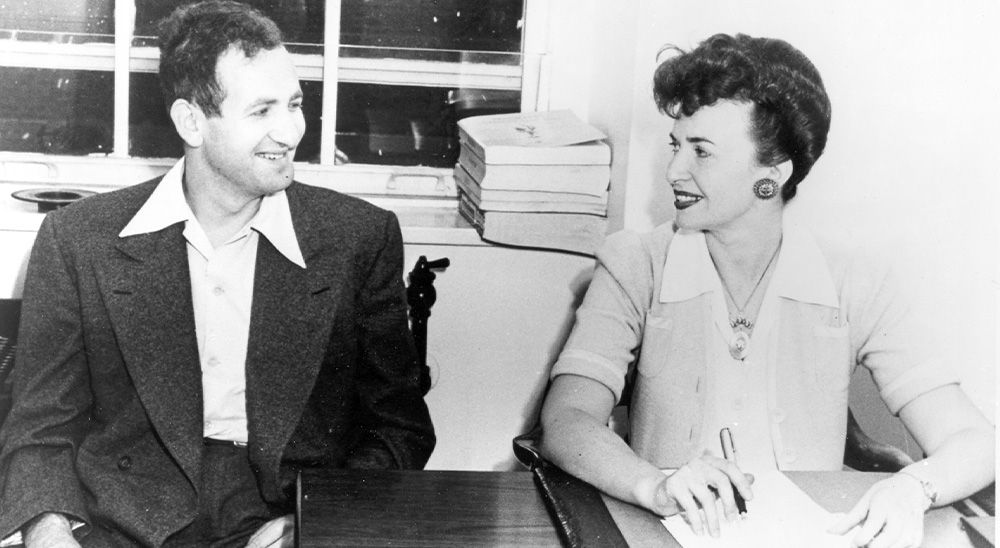 Bernard and Sylvia Lawry look at each other, smiling, as they sit at a table.