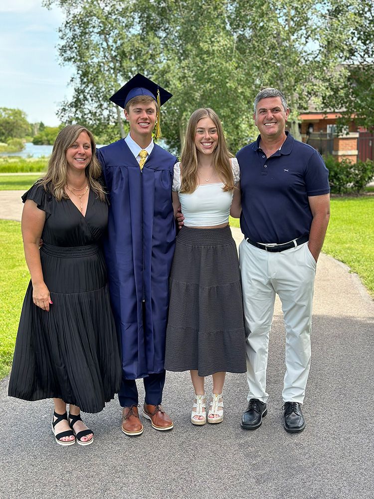 A family of four poses together. The teenage son wears a graduation cap and gown.
