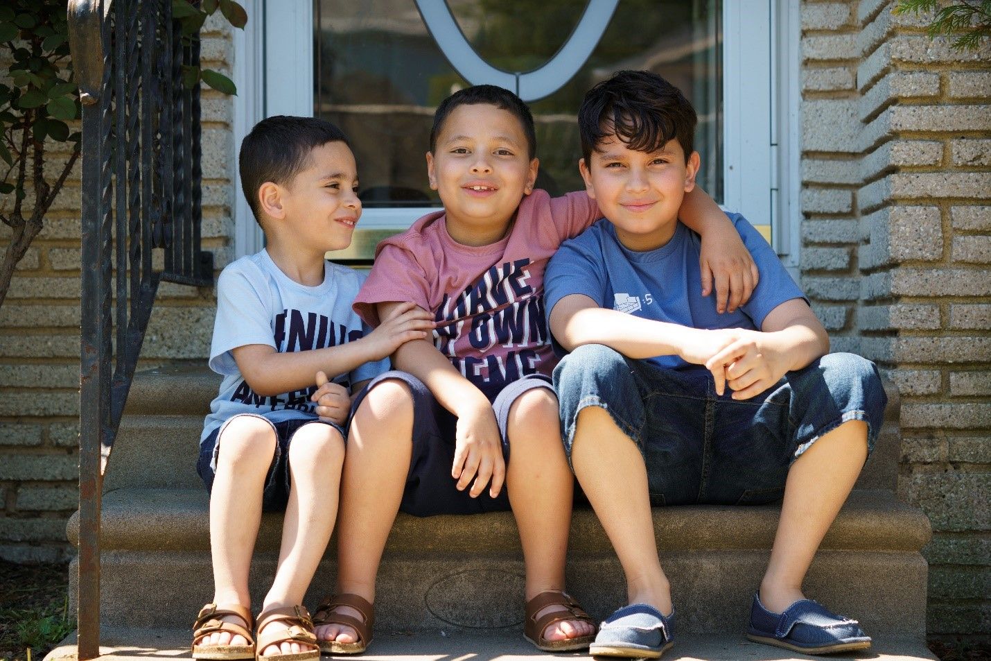 A boy who lives with MS sits on the stoop of his house between his two brothers.