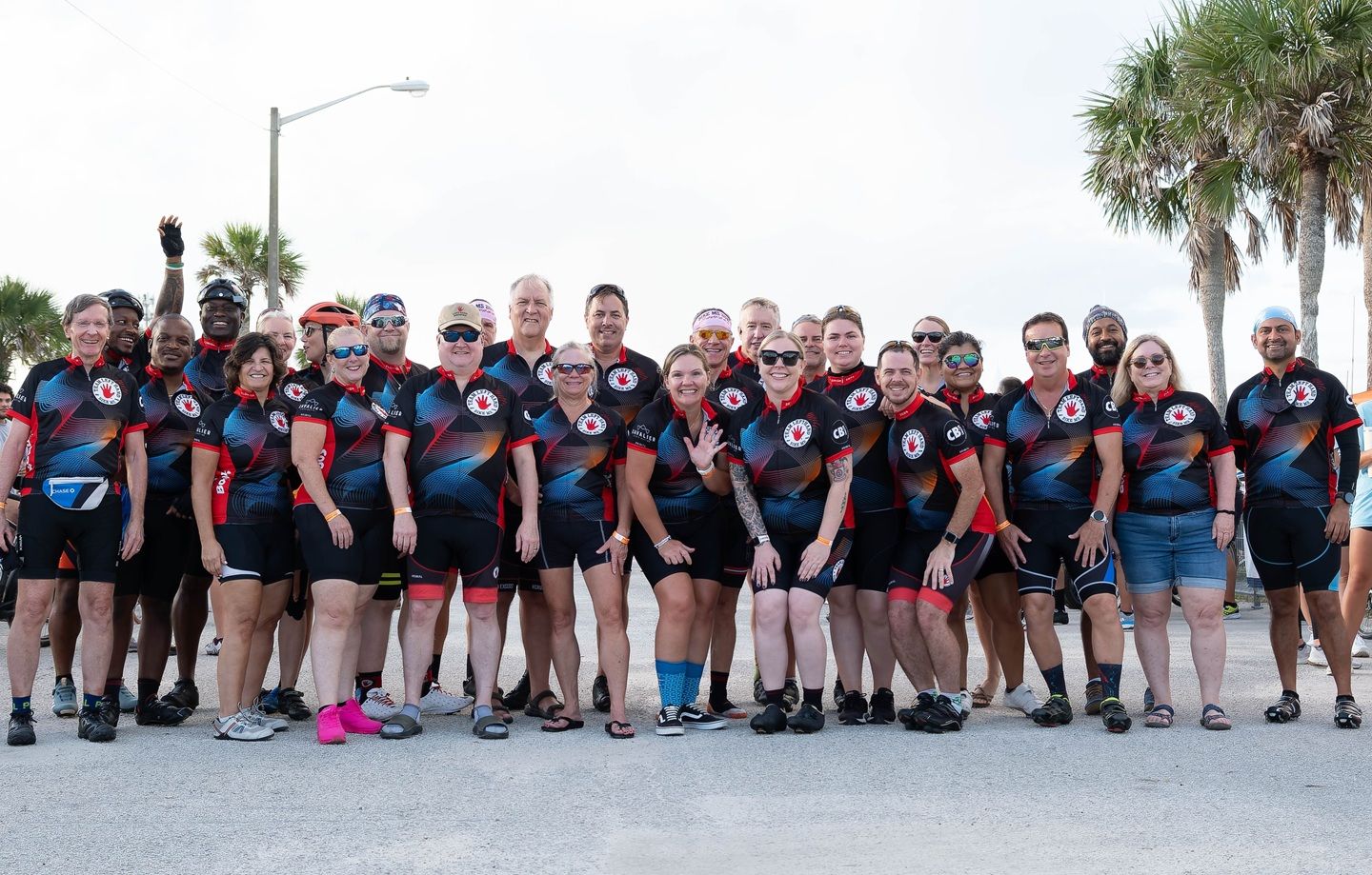 A group of 27 smiling members of Team Left Hand with matching uniforms poses in front of palm trees.