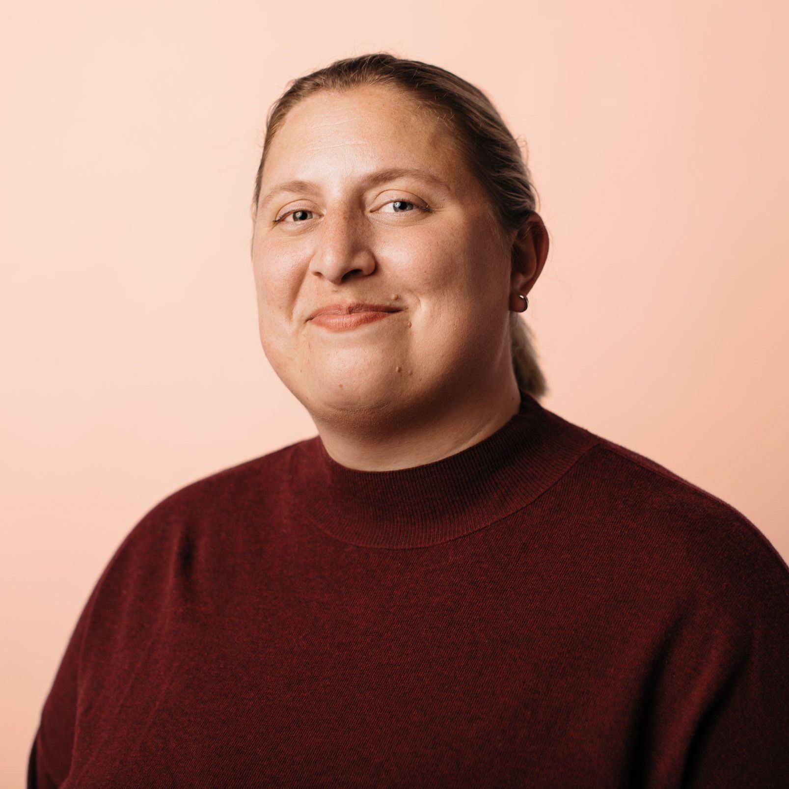 A headshot of a young, white woman against a salmon pink background.