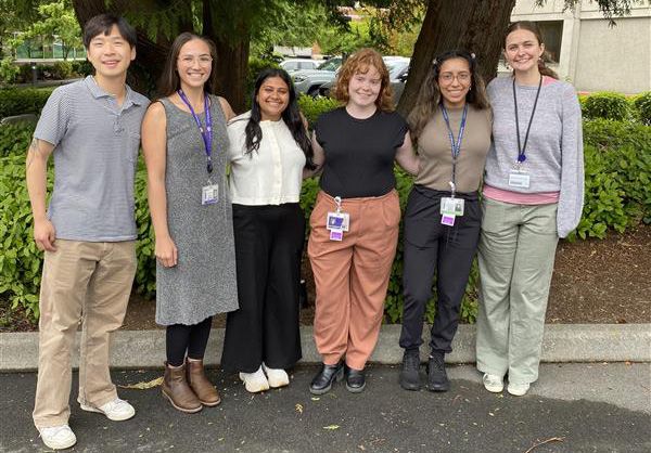 A group of 6 people stand together outside, smiling.