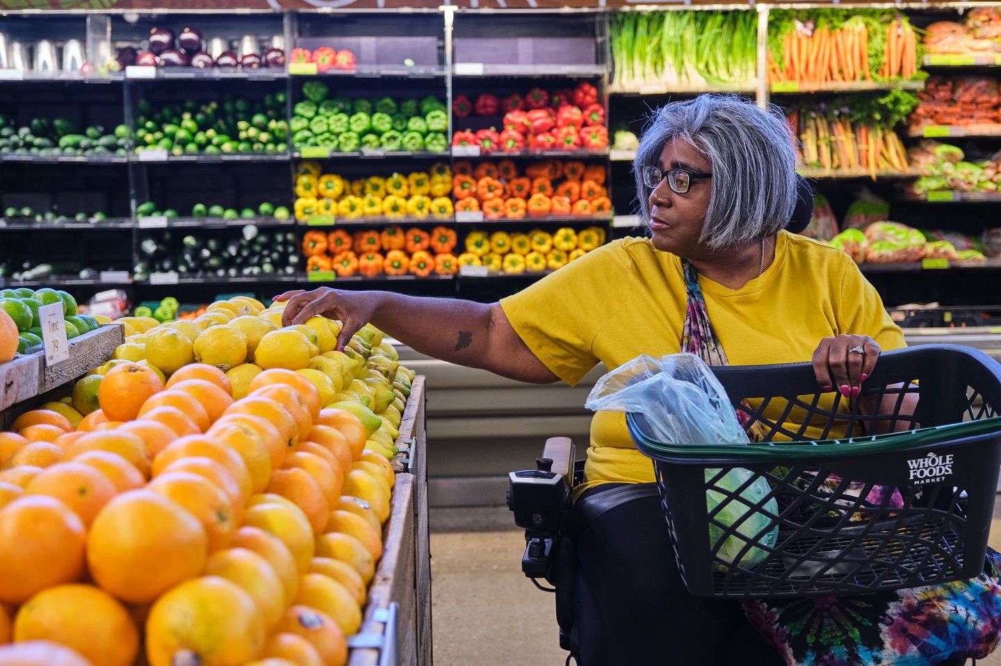 Stephanie, who lives with MS, uses her power wheelchair to shop for produce at her local grocery store.