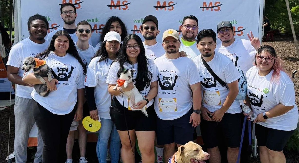 A group of people and three dogs pose together at Walk MS.