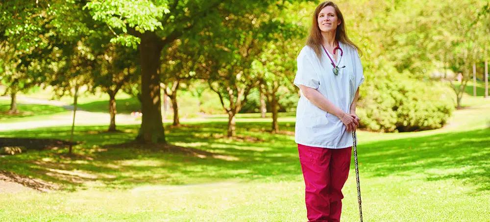 Debi Capwell in nurse scrubs holding a cane
