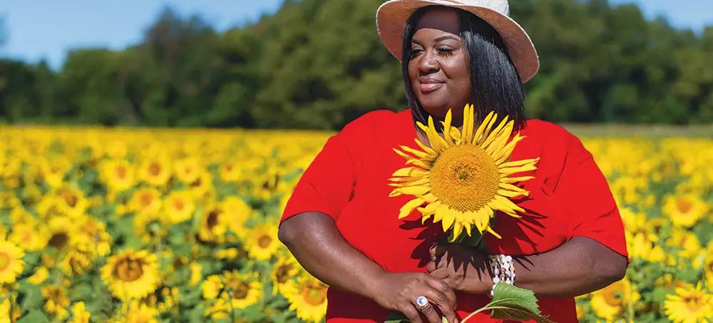 Nicole White holding a sunflower in a field of sunflowers
