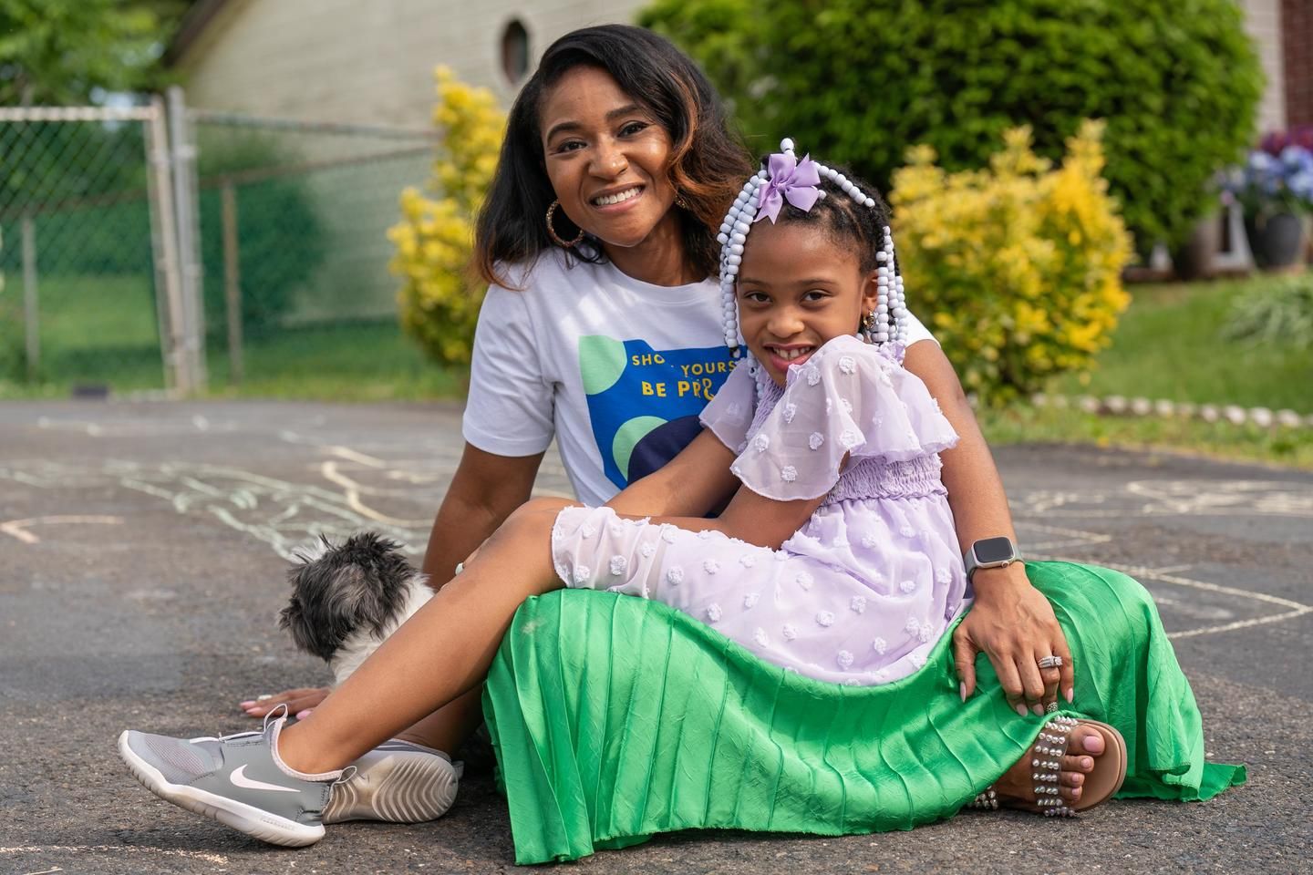 Kresence, a woman who lives with MS, sits on the driveway with her daughter on her lap, after playing hopscotch.